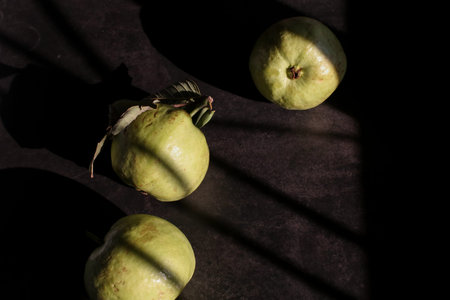 Guava fruit on a dark background with shadows from the sun.