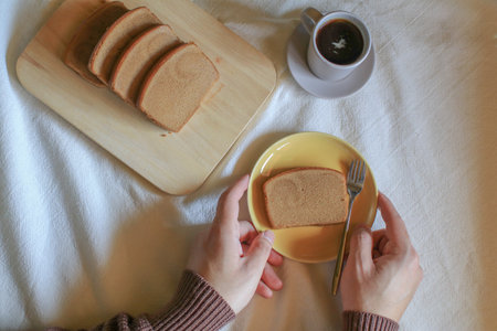 Hand holding homemade butter bread with coffee on white table. Vintage minimal tone. Breakfast time.の写真素材