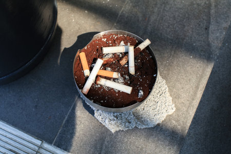 Ashtray with cigarettes butts under sunlight outdoor on street. Space for text. Unhealthy life style, Bad habits conceptの写真素材