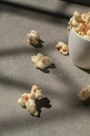 Popcorn in white cup under sunlight with shadow on grey background. Cinema snacks. Party time.の写真素材