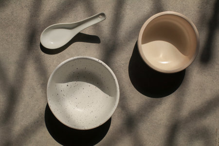 Two Empty blank white ceramic round bowl on grey background under sunlight with shadow. Traditional handcrafted kitchenware conceptの写真素材