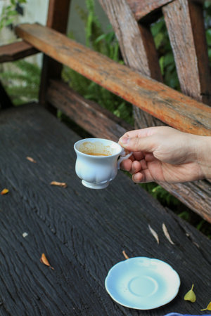Hand hold white coffee cup on wooden table with autumn leaves. Outdoor lifestyle. Refreshment summer drink with copy space.の写真素材