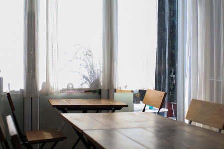 Wooden table, modern chairs and white curtain. Interior design of stylish dining room restaurant on background.の写真素材