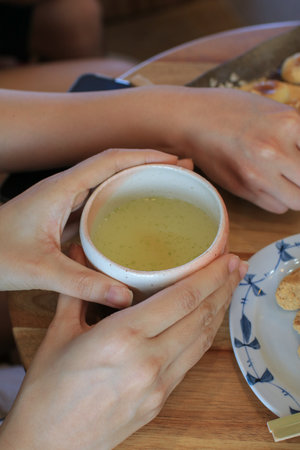 Woman hands hold cup of green tea on wooden table background in the japanese restaurant. Tea serving in a small vintage cupの写真素材