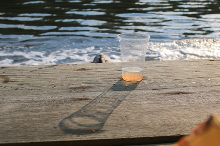 Plastic glass on wooden board with sunlight and shadow. Nature background. Environmental conservation.の写真素材
