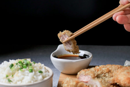 Hand use chopstick eating Japanese tonkatsu fried pork cutlet recipe with sweet sour sauce and rice on wooden broad. Asian food.の写真素材
