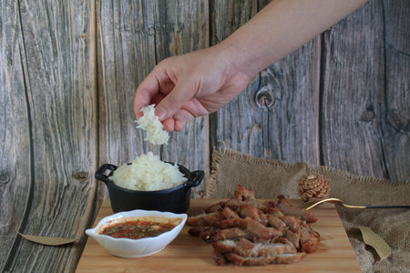 Grilled pork with dipping spicy sauce and sticky rice on wooden cutting board. Local street Thailand...