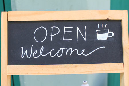 Open and welcome sign on blackboard outside coffee shop or restaurant. Welcoming customer.