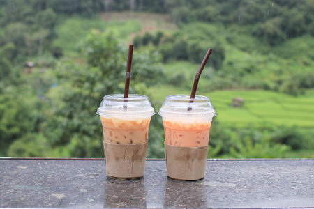 Iced thai tea with paper cup sleeve on the wooden table with green mountain view. Shop in nature.