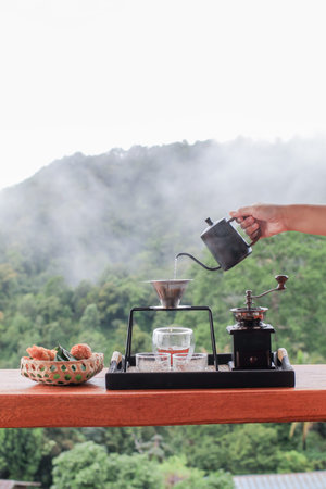 Hand pouring hot water on ground coffee with filter, barista using drip coffee set with mountain and...