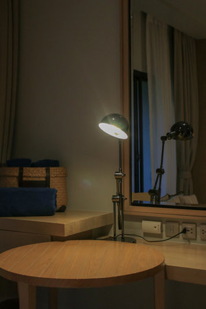 Table lamp on wooden table with mirror in cozy home. Bedside table with night light. Modern creative workspace backgroundの写真素材