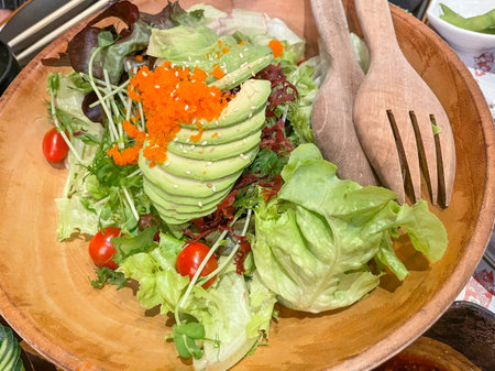 Healthy green salad with avocado, tobiko and fresh vegetables in wooden bowl. Healthy foodの写真素材