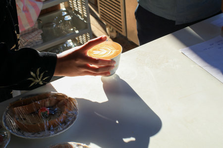 Barista making hot latte with foam milk art on counter in coffee shop under sunlight. Morning breakfast.の写真素材