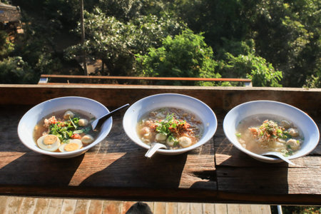 Rice vermicelli Noodle soup with pork balls and egg in white bowl on wooden terrace under sunlight.