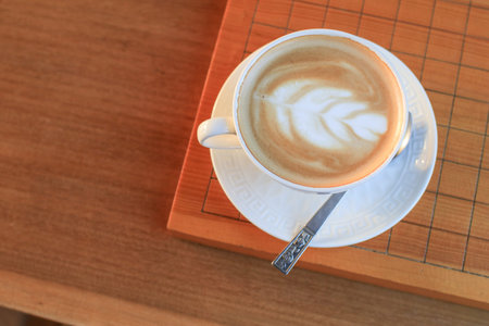 Hot coffee with foam milk latte art in white ceramic cup on wooden table. Refreshing morning.