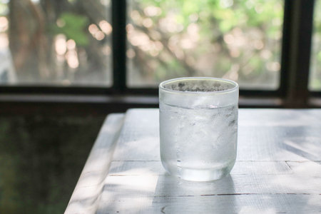 Glass of iced water with aesthetic sunlight shadows on white wooden table. Healthy summer beverage, copy space.の写真素材