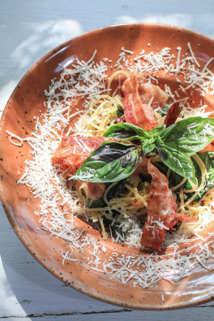 Spicy spaghetti with chili garlic, bacon and cheese in brown plate bath with sunlight, Delicious Italian food.の写真素材