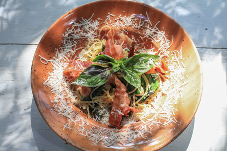 Spicy spaghetti with chili garlic, bacon and cheese in brown plate bath with sunlight.の写真素材