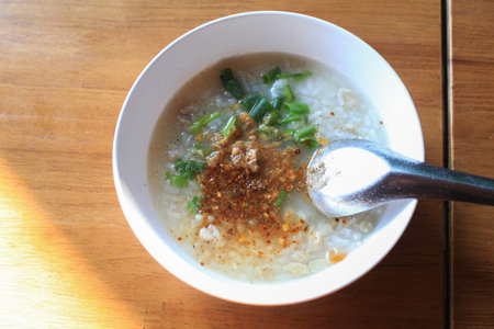 Boiled rice in white bowl on wooden table with morning sunlight. Asian breakfast style. Pork Porridge.の写真素材