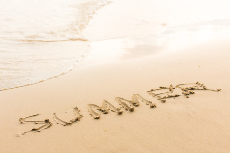 "Summer" ; written in the sand on the beach with blue waves in the background.の写真素材