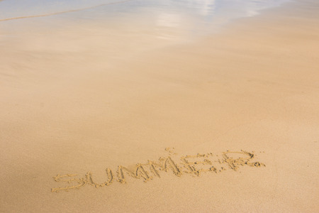 "Summer" ; written in the sand on the beach with blue waves in the backgroundの写真素材