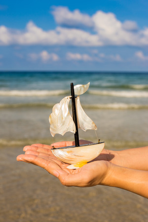 Summer vacation concept. Toy sailing boat in hands on the water background.の写真素材