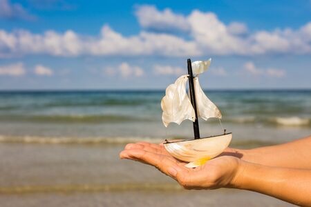 Summer vacation concept. Toy sailing boat in hands on the water background.の写真素材