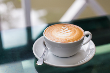 A glass of hot coffee latte with latte art on green glass table.の写真素材