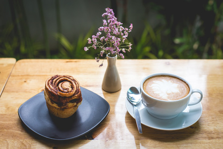 cinnamon bun and art latte on wooden table, nature background, retro and vintage style.の写真素材