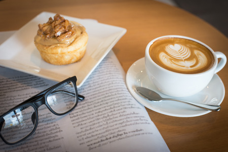 Apple cinnamon roll served with latte art coffee and newspaper on the table at restaurant black and white toneの写真素材