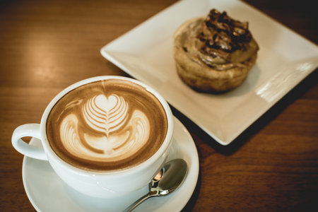 Apple cinnamon roll served with cappuccino coffee on the table at restaurant.