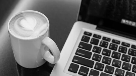 Hot art Latte Coffee in a cup and laptop on wooden table in Coffee shop image.の写真素材