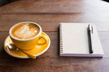 Hot latte art coffee cup on wooden table and note book