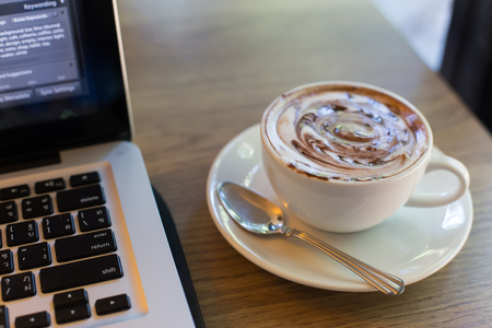 Hot art Latte Coffee in a cup and laptop on wooden table.の写真素材