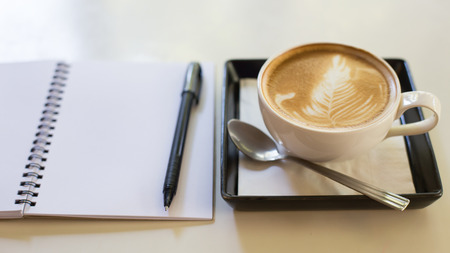 Hot latte art coffee cup on wooden table and note book.の写真素材