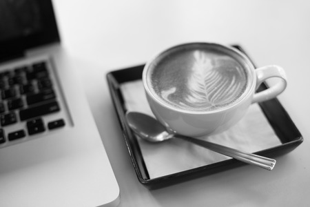 Hot art Latte Coffee in a cup and laptop on wooden tableの写真素材