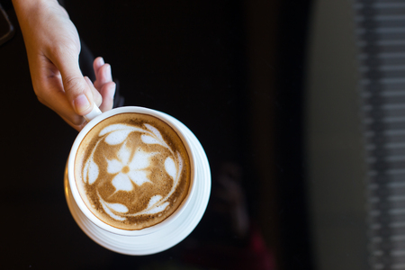Woman holding cup of coffee latte, with heart shape.の写真素材