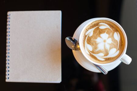 Hot latte art coffee cup on wooden table and note bookの写真素材