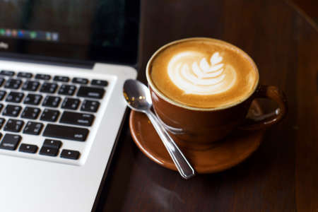 Hot art Latte Coffee in a cup and laptop on wooden table.の写真素材
