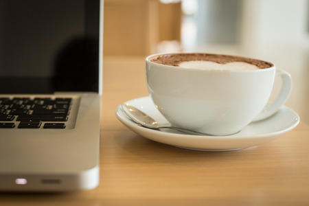 A cup of coffee in a white cup and computer labtop on mable tableの写真素材