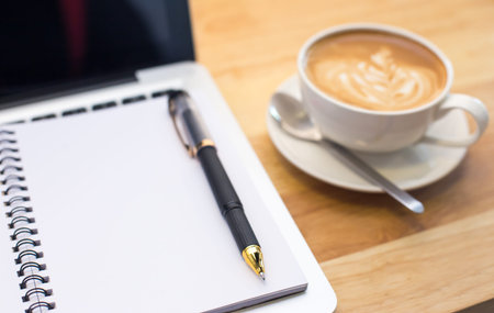 Coffee cup and notebook on table background.