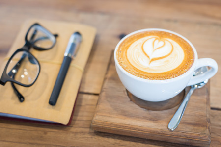 Hot latte art coffee cup on wooden table and note book, vintage and retro styleの写真素材
