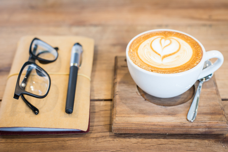 Hot latte art coffee cup on wooden table and note book, vintage and retro styleの写真素材