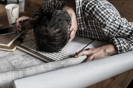 tired engineer lying and sleeping on blueprint with dark retro style.の写真素材