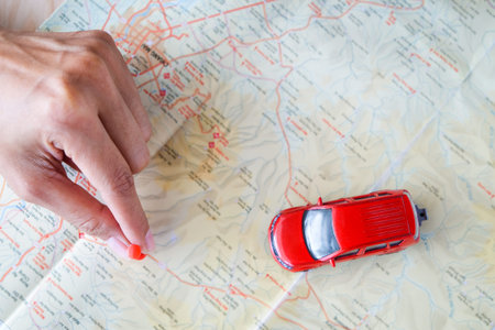 close up on a hand placing a pin on a map and car toy mark where to go