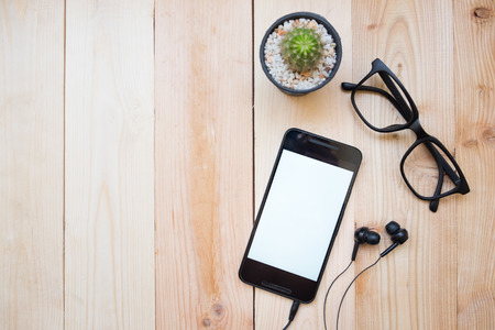 Close up of mart phone empty white screen and material office desktop on wooden desk top viewの写真素材