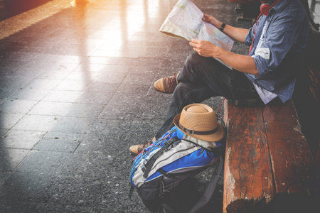 Side portrait of a  young man traveler sitting with map choose where to travel and bag waiting for...