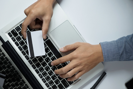 Man holding credit card in hand and entering security code using laptop keyboardの写真素材