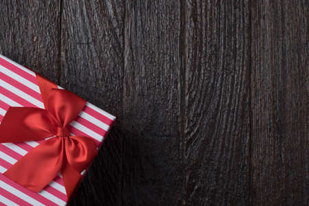 One gift box with an red big ribbon on old wooden dark brown background for christmas, close up view holidays concept, orizontal versionの写真素材
