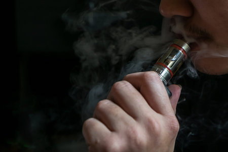 Man with concealed identity smoking a controversial vaping an electronic cigarette. Vaping is...